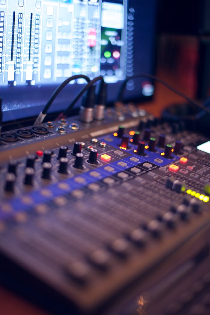 services-02 Close-up of a professional audio mixing console with glowing LED indicators.