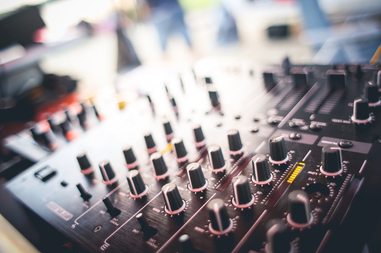 home-hero A close-up shot of a DJ mixing panel with various knobs and sliders in a blurred background setting.