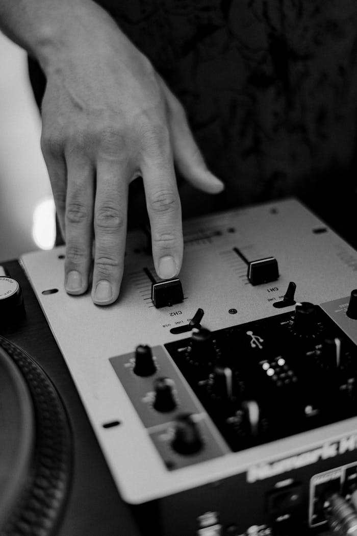 services-04 Close-up of a hand on a DJ mixer in black and white, capturing sound mixing art.
